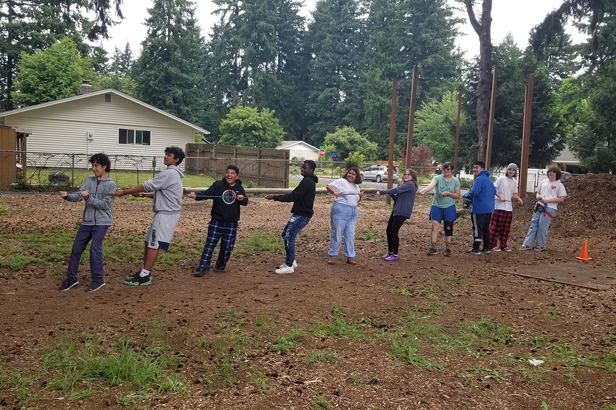 Student pull on a rope to hoist their fellow teammates up in the challenge course.