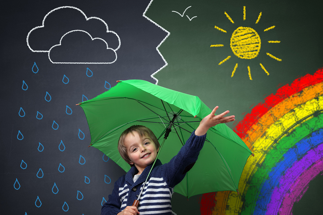 Child holding an umbrella standing in front of a chalk drawing of changing weather from rain storm to sun shine with a rainbow on a school blackboard