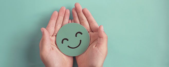 hands holding a paper green smiley face